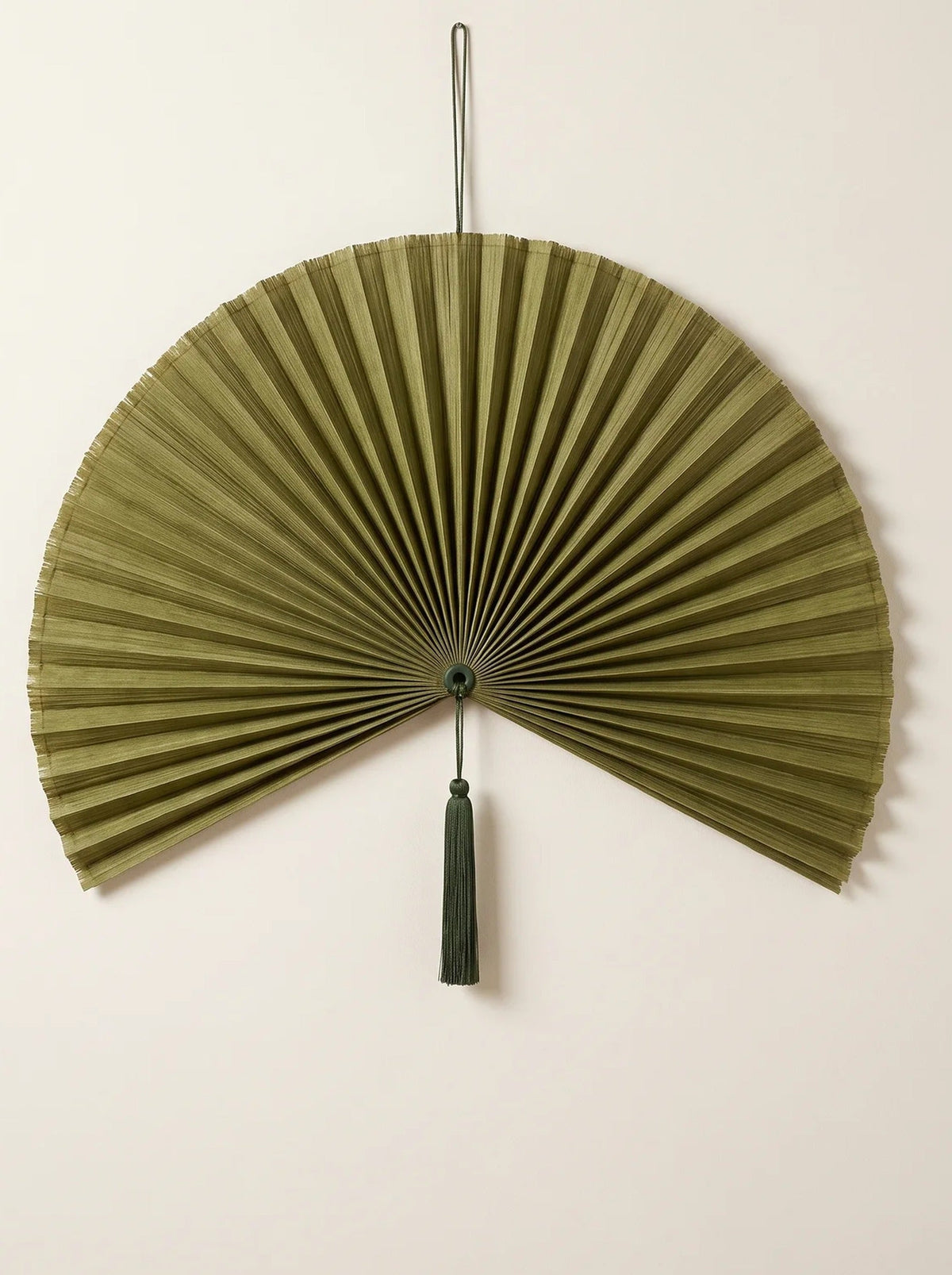 Moss green pleated bamboo hanging wall fan with a matching green tassel on a cream wall
