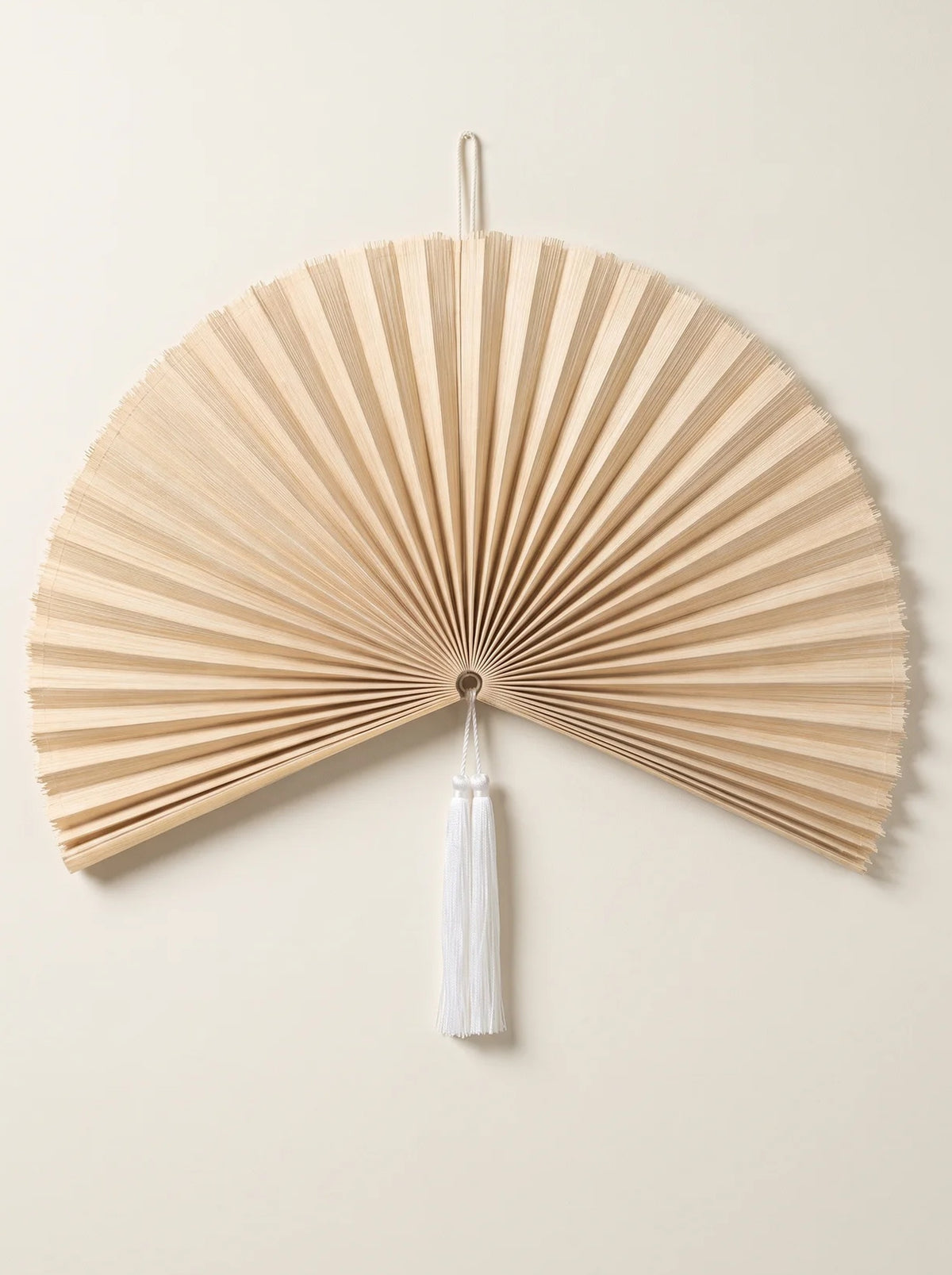 Natural Bamboo pleated hanging wall fan with a white tassel on a cream wall