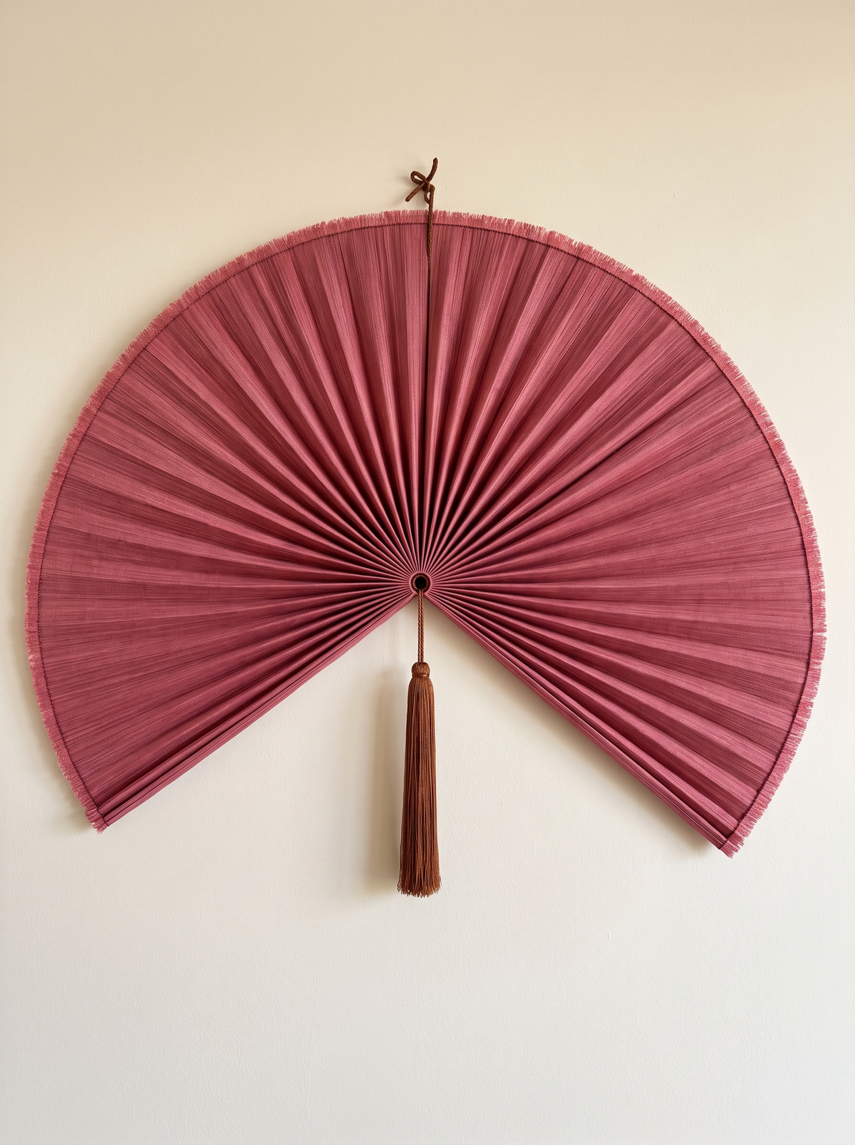 Magenta hanging wall fan with pleated panel and brown tassel on a cream wall